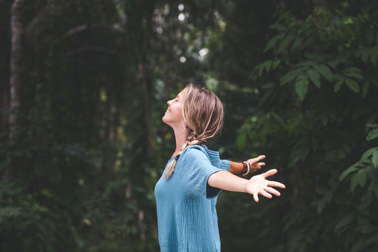 gratitute-recovery-750×500 woman standing in a forest with her arms out expressing gratitude.