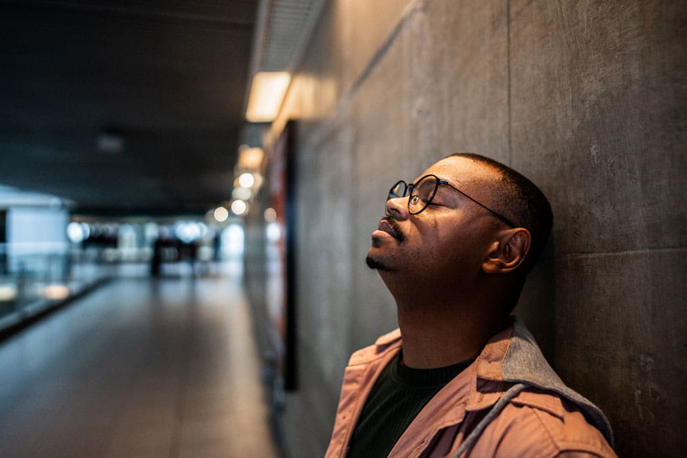 man leaning against a wall looking upset and defeated.