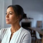 Looking out (1000 x 667 px) A woman stands indoors looking thoughtfully out of a window, with natural light illuminating her face.