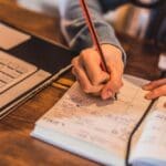 Schedule (1000 x 667 px) A person writing in a planner next to an open laptop, organizing their schedule and creating a routine.