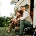 A couple sitting outside a caravan on a grassy field surrounded by trees. The couple is exploring how nature and outdoor activities can support mental health in recovery