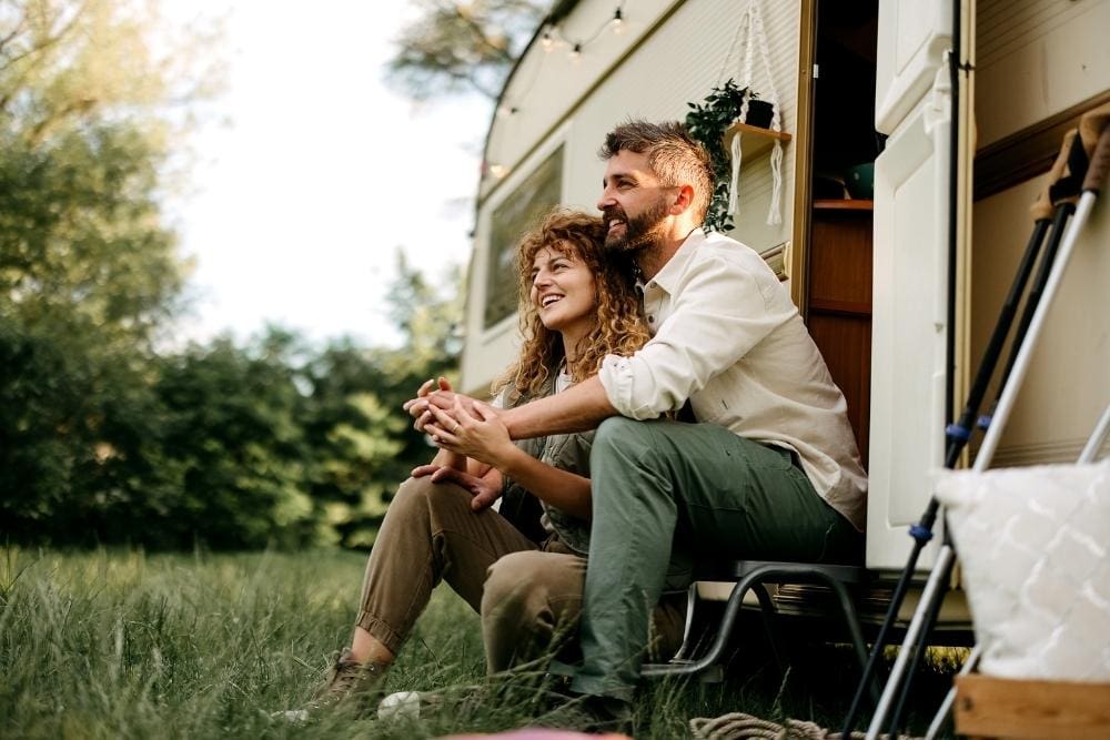A couple sitting outside a caravan on a grassy field surrounded by trees. The couple is exploring how nature and outdoor activities can support mental health in recovery